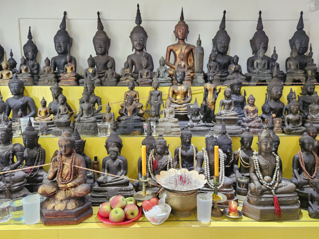 Large Buddhist prayer altar with dozens of Buddha statues in various styles and postures, arranged for regular worship and offerings
